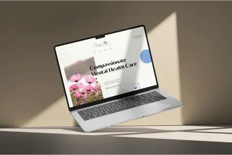 Laptop displaying a website for compassionate mental health care, featuring floral imagery and a clean layout, emphasizing professional online presence for therapists and wellness coaches.